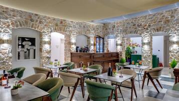 A restaurant with stone walls, green upholstered chairs, and tables with wine glasses and bottles.
