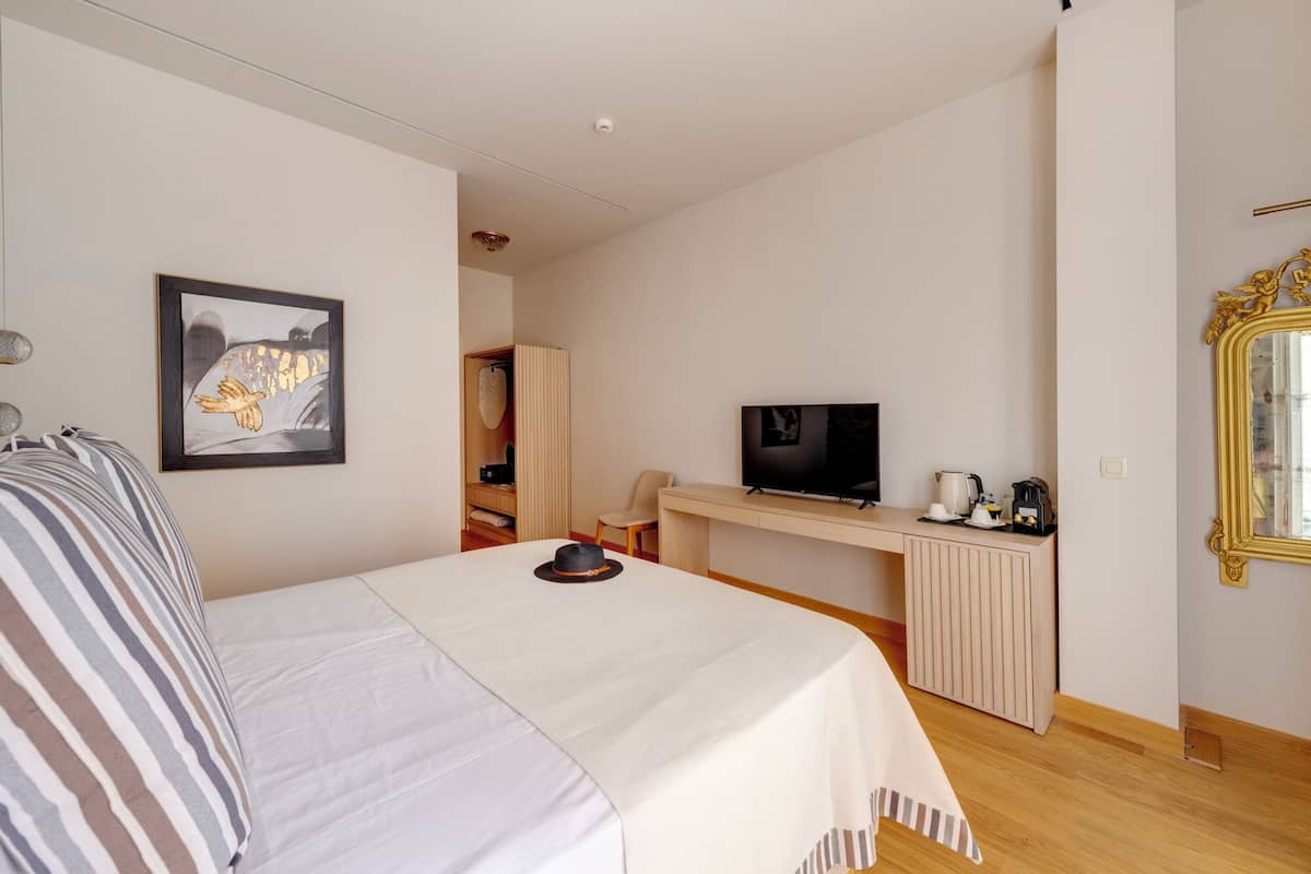 A hotel room with a bed, a desk with a TV, a wardrobe, and a bathroom visible through an open door.