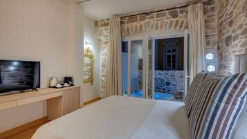 Een slaapkamer met een groot bed, een televisie en uitzicht op een stenen muur en een deur naar een balkon.