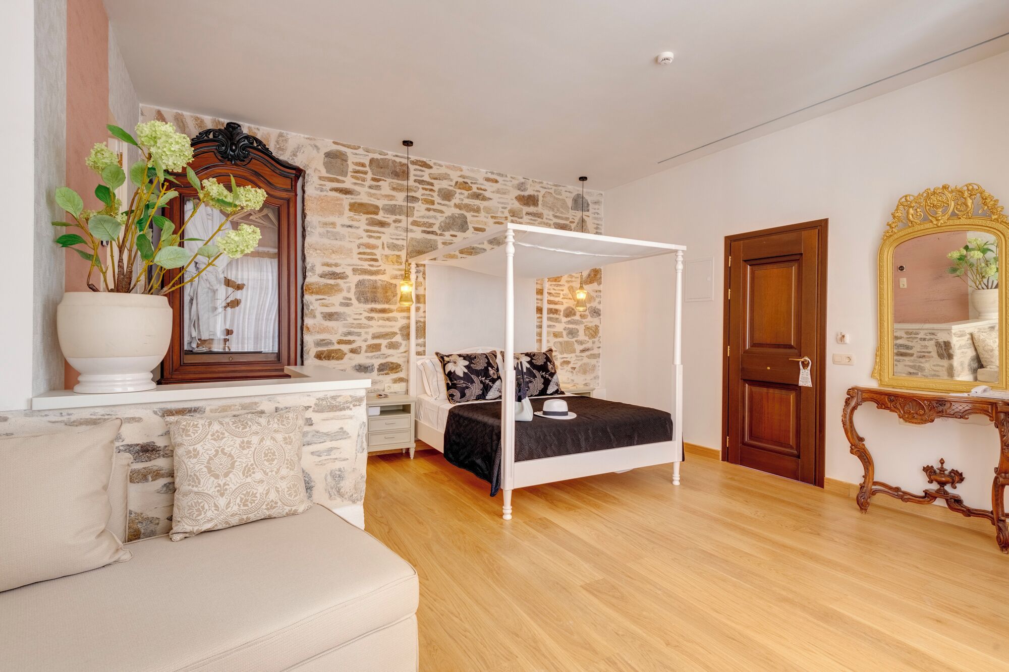 Een slaapkamer met een hemelbed, een stenen muur, een houten deur en een spiegel met een gouden lijst.