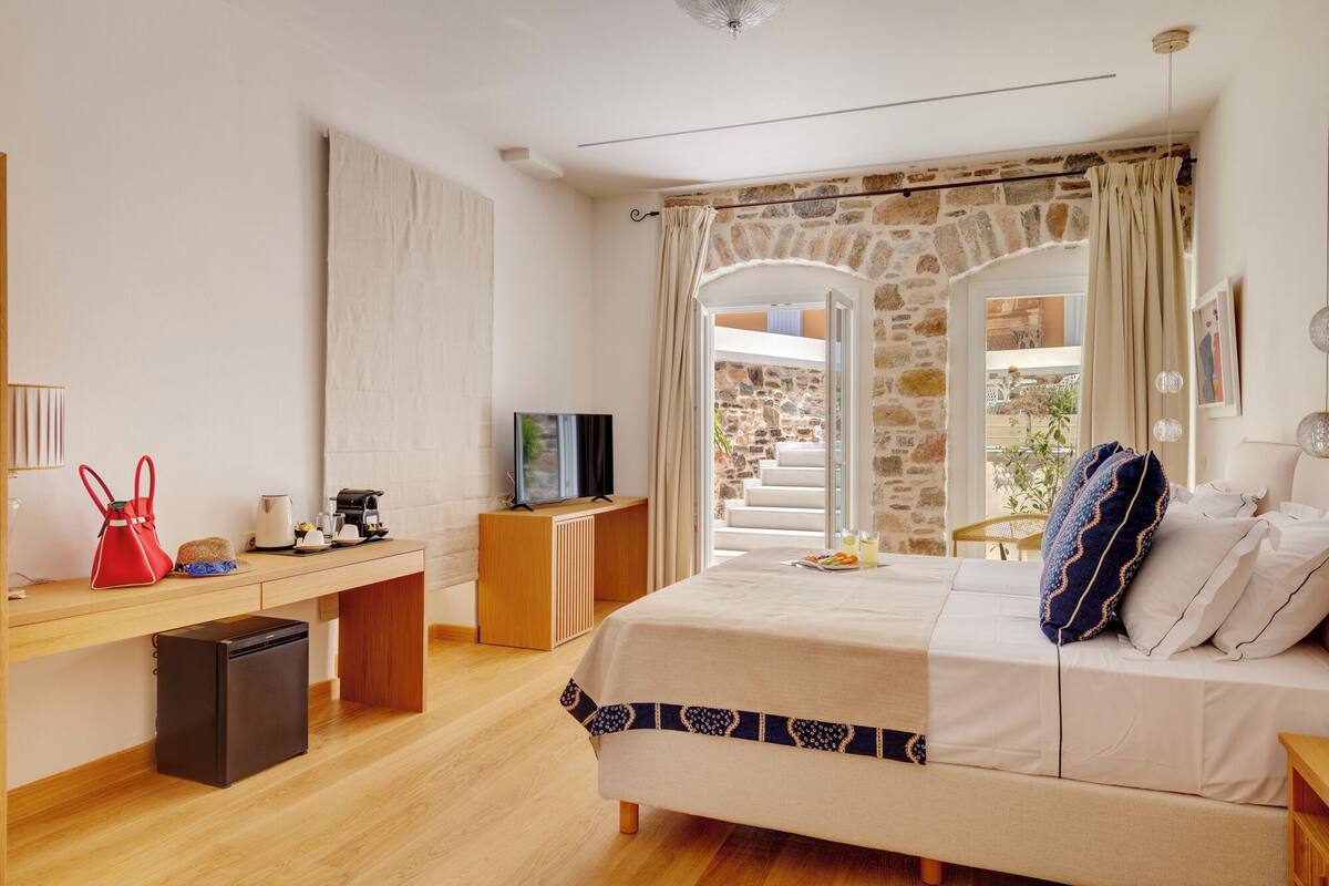 A bedroom with a bed, a desk with a TV, a coffee machine, and a view of the outside.