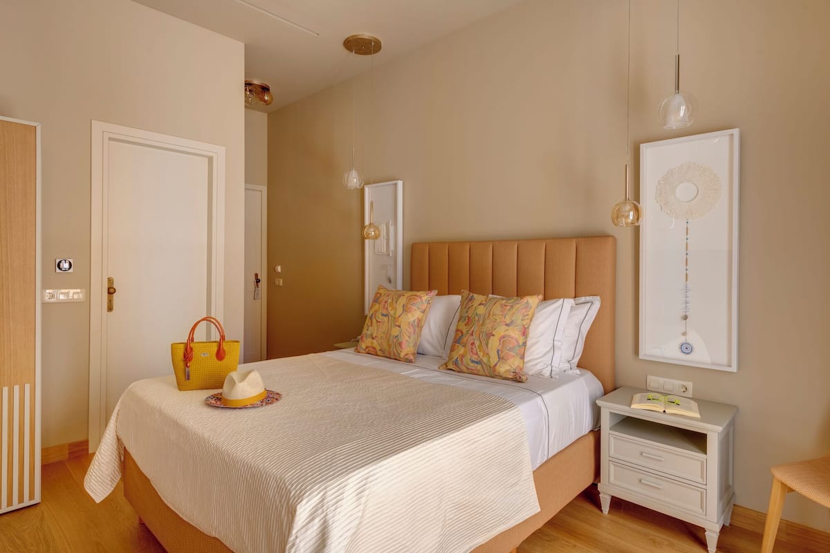 A bedroom with a bed, bedside tables, a nightstand, a hanging light fixture, and a wall-mounted artwork.