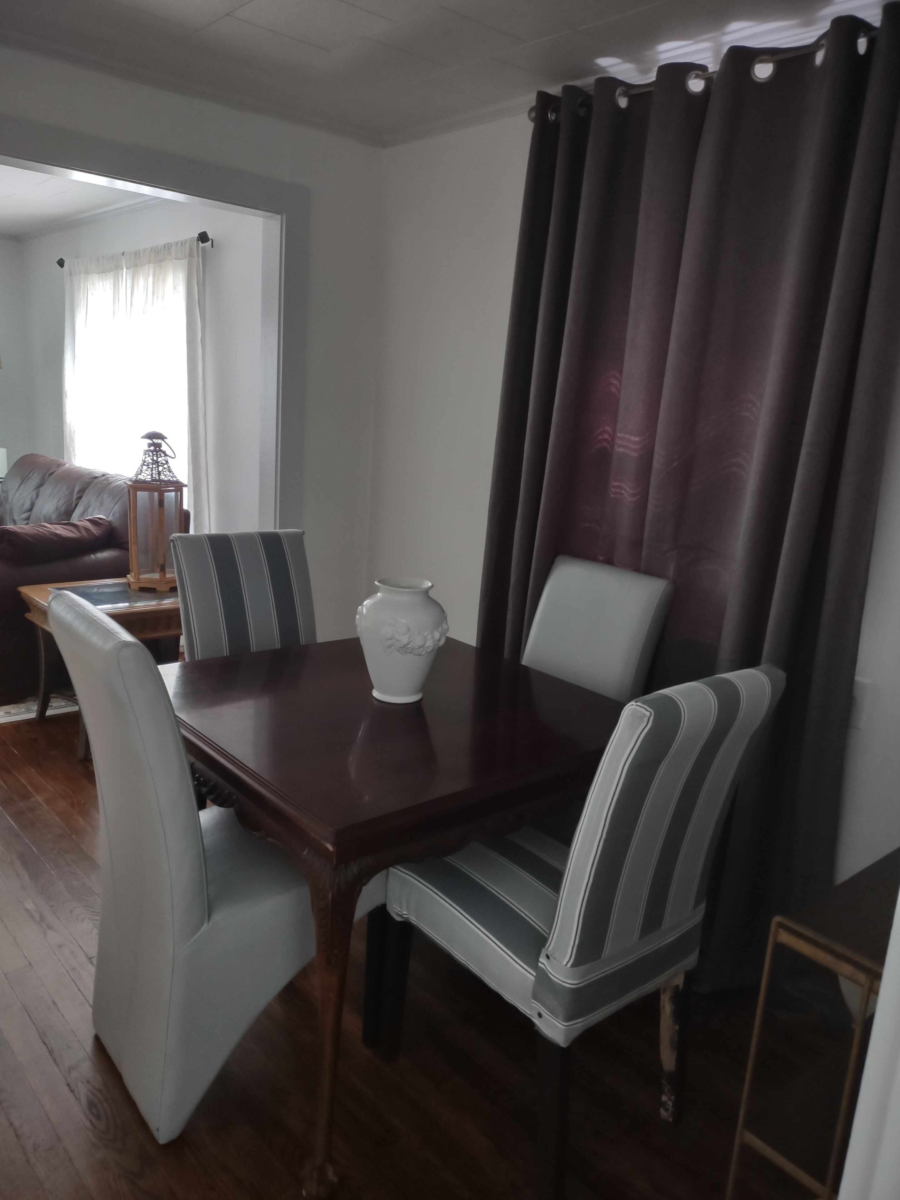 A dining area with a wooden table, striped chairs, and a white vase.