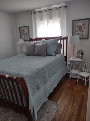 Una camera da letto con un letto di legno, un comodino, una sedia, una lampada e una finestra con tende.