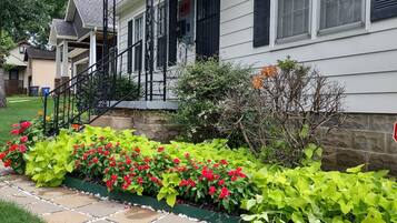 A house with a porch, steps, and a garden with red and green plants.