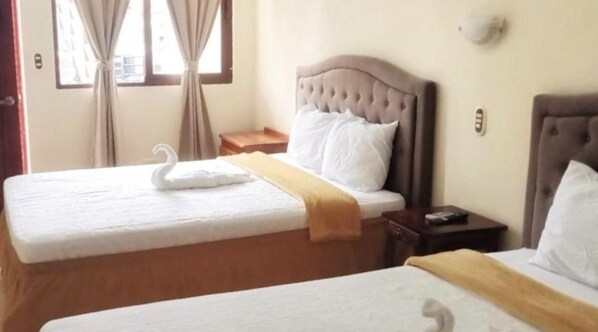 A hotel room with two beds, each with a white bedspread and a swan-shaped pillow. There is a wooden nightstand between the beds with a remote control on it. - Hotel Maria Ofelia (San Luis Talpa)