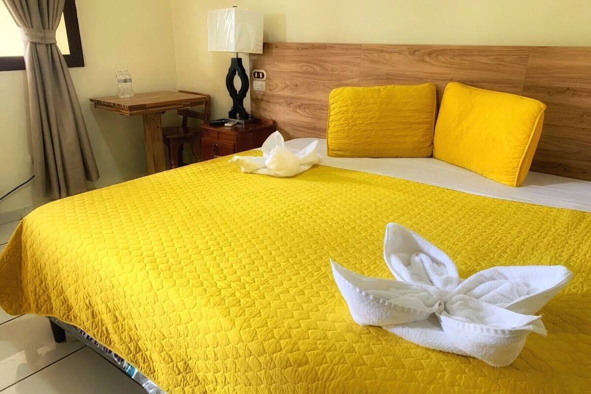 A hotel room with a large bed, a wooden headboard, a nightstand with a lamp, and a small table with a glass of water.