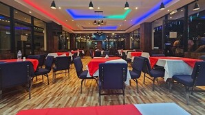 Un restaurante con varias mesas y sillas, suelo de madera e iluminación colgante.