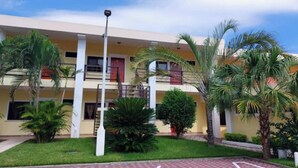 Un hotel de varios pisos con un patio central, palmeras y un camino de baldosas rojas.