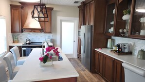 A kitchen with wooden cabinets, a white countertop, a stainless steel refrigerator, and a coffee machine.