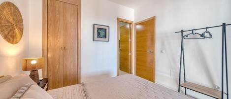 Un dormitorio con cama, armario de madera, un cuadro enmarcado en la pared y un tendedero.