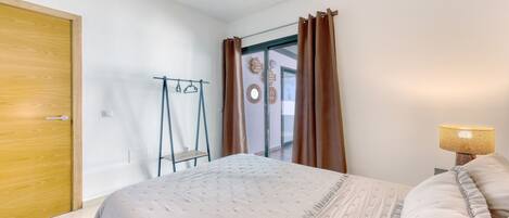 Une chambre à coucher avec un lit, une lampe de chevet, une porte en bois et une vue sur l’extérieur.