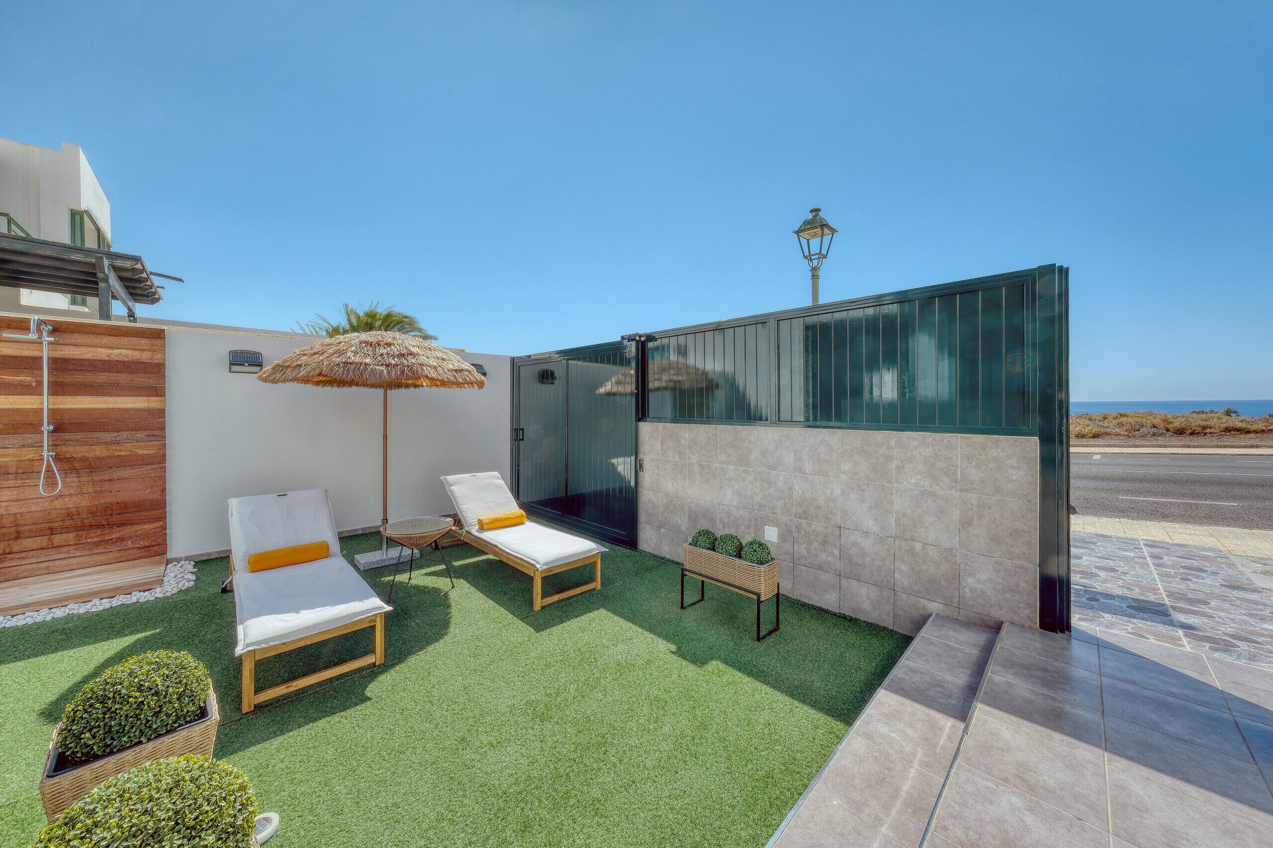 A modern outdoor lounge area with two sunbeds, a thatched umbrella, and a small table with potted plants.