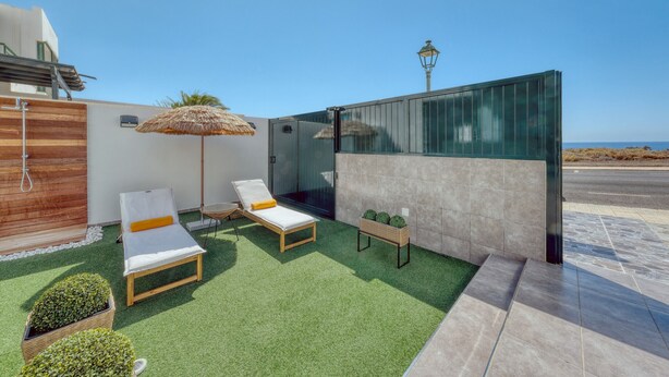 Et moderne udendørs loungeområde med to liggestole, en stråparasol og et lille bord med plantekrukker.