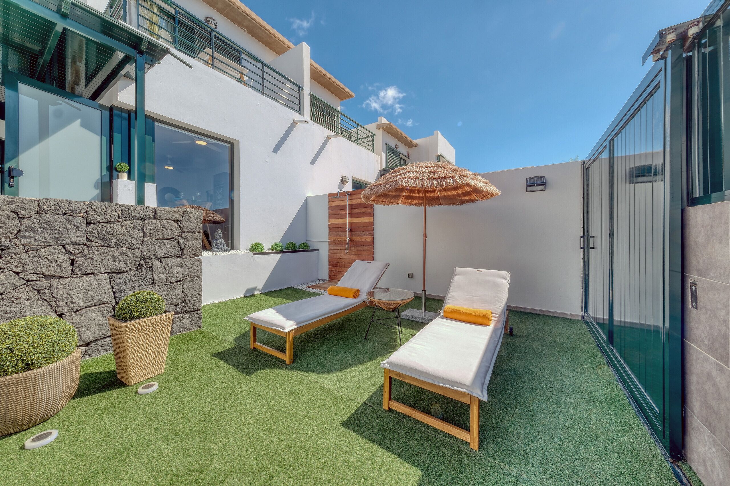 A modern outdoor area with two sun loungers, a thatched umbrella, and a stone wall.