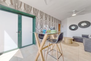Una sala moderna con una mesa de comedor de vidrio, un sofá gris y dos espejos colgantes.