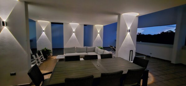 Une terrasse extérieure avec une table à manger, des chaises, un canapé et une grande fenêtre.