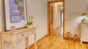 A hallway with a wooden floor, a framed poster, a potted plant, a small cabinet, and wicker baskets. - Costa do Sol, a Home in Madeira (Funchal)