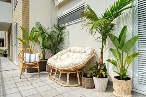 A wicker chair with a cushion, a potted plant, and a window on a balcony. - Costa do Sol, a Home in Madeira (Funchal)