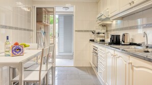 A kitchen with white cabinets, a countertop, and a dining area with chairs and a table. - Costa do Sol, a Home in Madeira (Funchal)