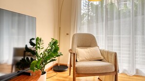 A modern living room with a flat-screen TV, a beige armchair, a floor lamp, and a potted plant. - Costa do Sol, a Home in Madeira (Funchal)