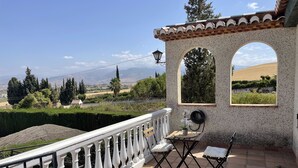 A terrace with a white balustrade, a small table with a chair, and a view of the countryside. - Granada Sights (AN)