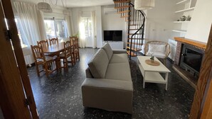 A living room with a sofa, dining table, chairs, a TV, a fireplace, and a spiral staircase. - Granada Sights (AN)