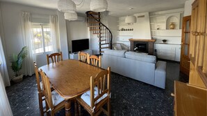 A modern living room with a wooden dining table, a sofa, a fireplace, and a spiral staircase. - Granada Sights (AN)