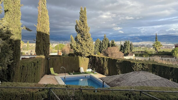A pool area with a view of a cityscape, surrounded by tall trees and a cloudy sky. - Granada Sights (AN)