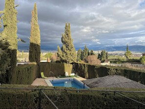 A pool area with a view of a cityscape, surrounded by tall trees and a cloudy sky. - Granada Sights (AN)