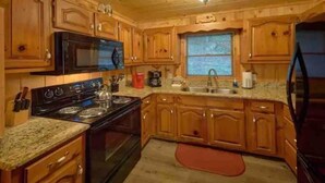 Una cucina con mobili in legno, un piano cottura nero, un forno a microonde e un frigorifero.