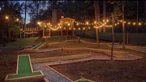 Un campo da minigolf con una casa sullo sfondo, circondato da alberi e luci decorative.