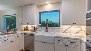 Een moderne keuken met witte kasten, een marmeren aanrechtblad en uitzicht op de buitenlucht door een groot raam.