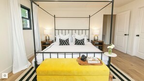Een hemelbed met een geel poufje, witte beddengoed en gestreepte kussens.