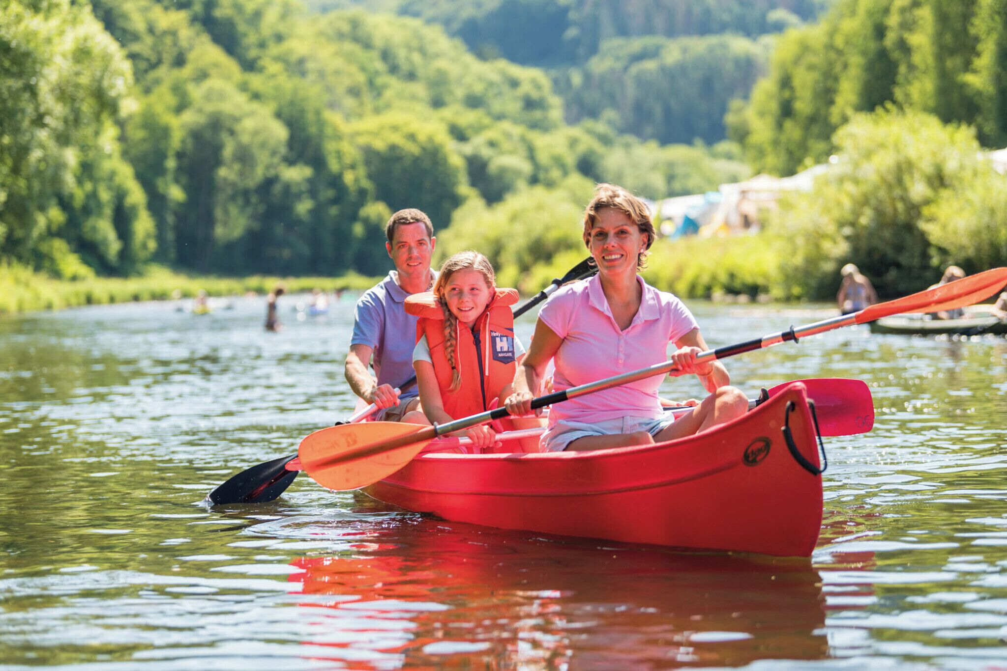 A family in a red kayak on a calm river surrounded by lush greenery.