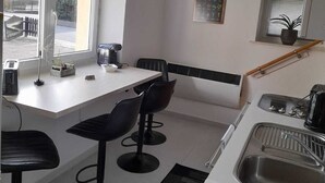 Eine moderne Küche mit weißer Arbeitsplatte, schwarzen Barhocker, einem Fenster, einer Uhr und einem Blumentopf.
