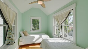 Una habitación con dos camas, ventilador de techo, ventana con cortinas y vistas al exterior.