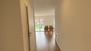 A hallway with wooden flooring leading to a dining area with a table and chairs. - Ferienwohnung in Ravensburg, Neubau, Ruhig, in der Natur, Barrierefrei, Terrasse (Ravensburg)