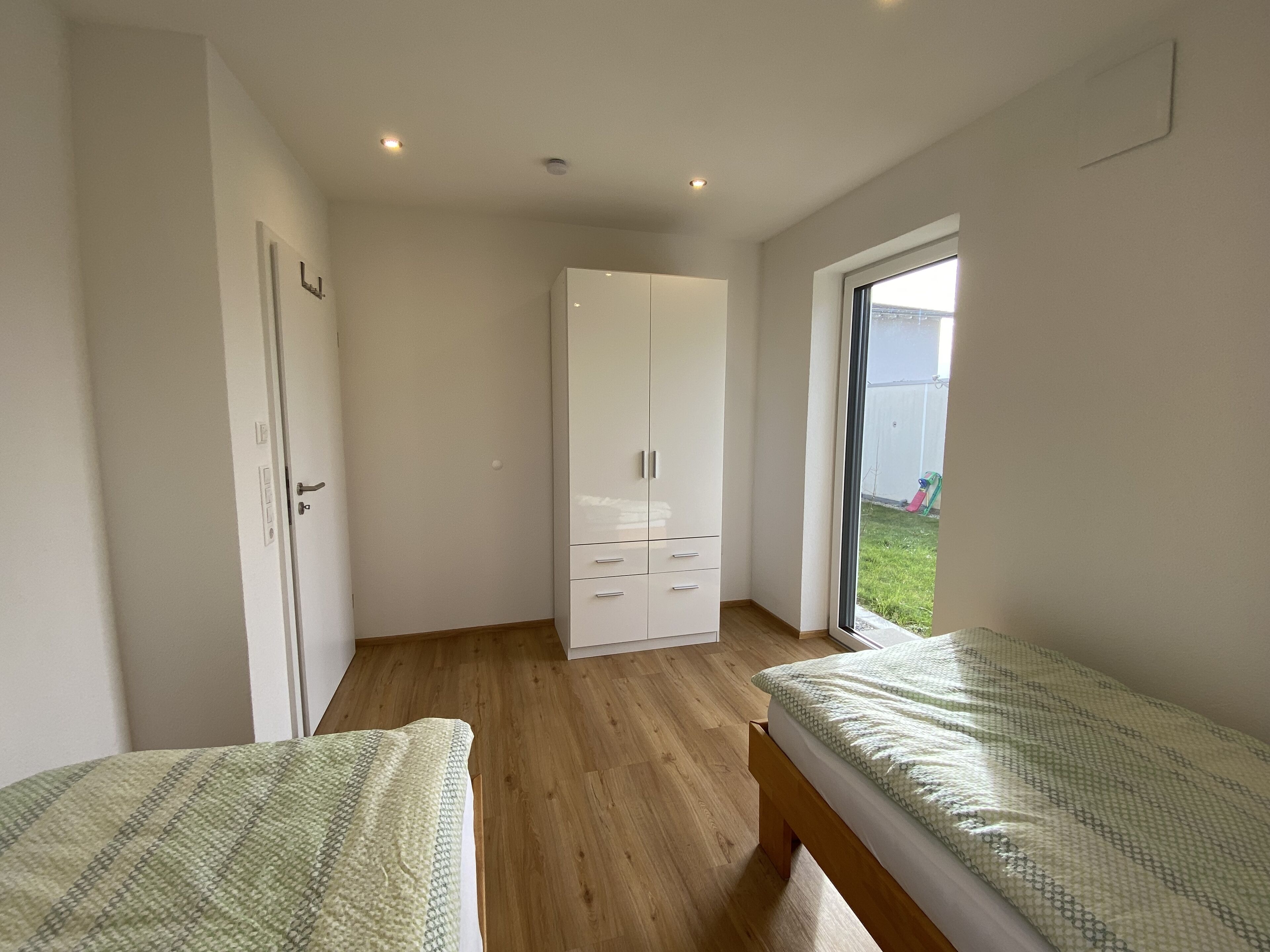 Un dormitorio con dos camas individuales, un armario y una puerta corrediza de vidrio al exterior.