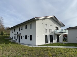Ein zweistöckiges Gebäude mit Balkon, einem kleinen Anbau und einem Rasen.