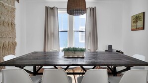 A dining area with a dark wooden table, white chairs, a hanging light fixture, and a window with curtains. - Charming Home and Cottage in Downtown St Augustine for 14 (St. Augustine)