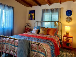A bedroom with a metal bed frame, colorful bedding, a bedside table with a lamp, and a wall-mounted mirror. - Lookout Cabin - Prescott Cabin Rentals (Prescott)