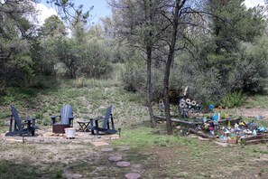 An outdoor area with Adirondack chairs, a fire pit, and a garden with various sculptures and plants.