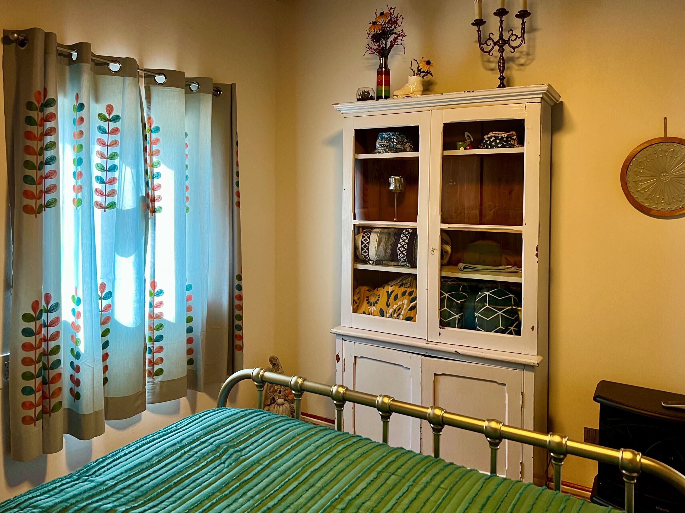 Un dormitorio con cama, armario, radiador y ventana con cortinas.