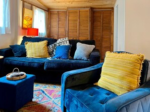 Una sala de estar acogedora con un sofá y un sillón a juego en tono azul oscuro, y una mesita auxiliar pequeña. Se observa también una alfombra colorida y un mueble de madera con puertas correderas.
