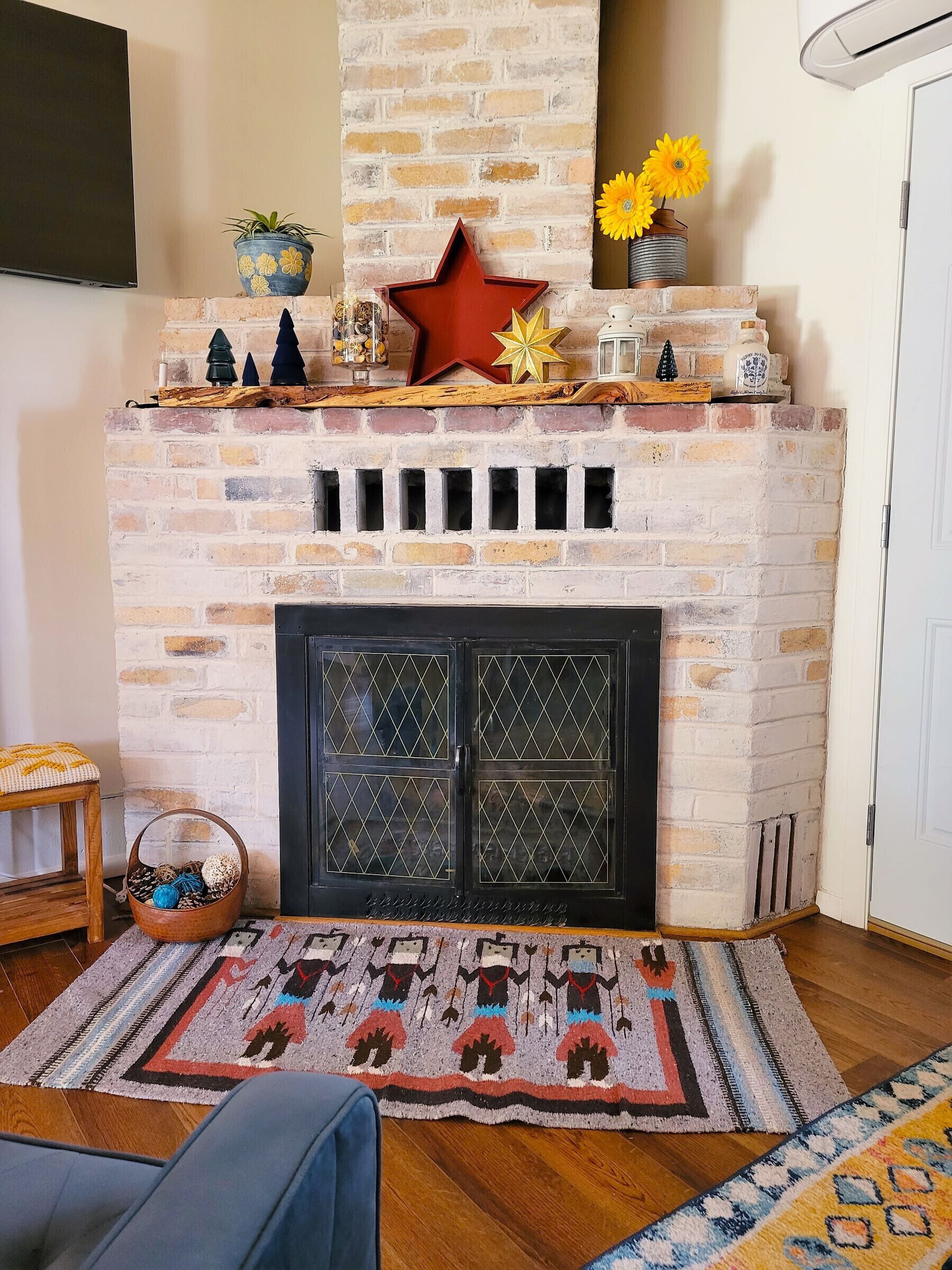Ein Kamin aus Ziegelsteinen mit Dekorationselementen, ein an der Wand befestigter Fernseher und ein gemustertes Teppich.