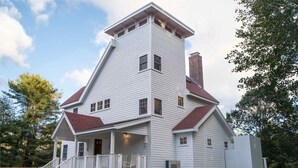 Ein zweistöckiges Haus mit einem steilen Satteldach, einer Veranda mit Geländer und einem Schornstein.