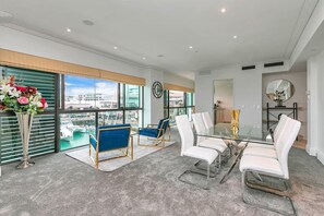 A modern room with a glass table, white and blue chairs, a large window with a view of boats, and a vase with flowers.