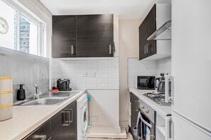 Compact kitchen with dishwasher, microwave, and gas stove, featuring a sink and ample natural light.