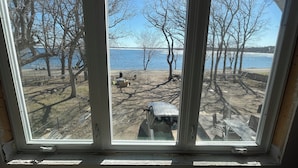 Une fenêtre donnant sur un espace au bord du lac, avec des arbres et un banc.